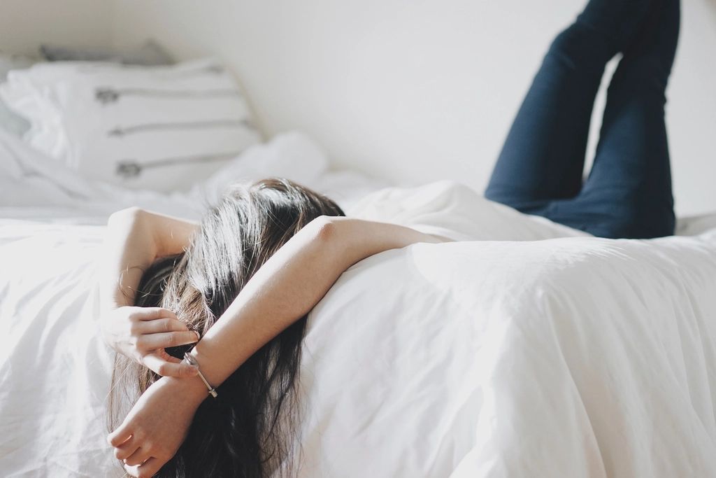Someone lying face down across a white bed, arms over their head.
