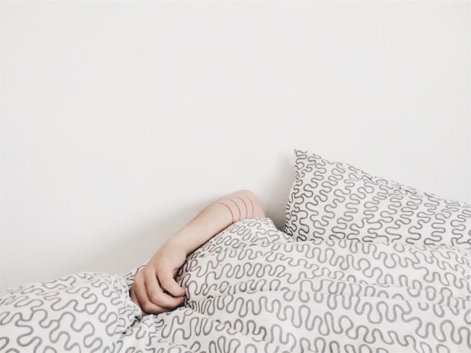 An arm wrapped around a patterned pillow on a white bed.